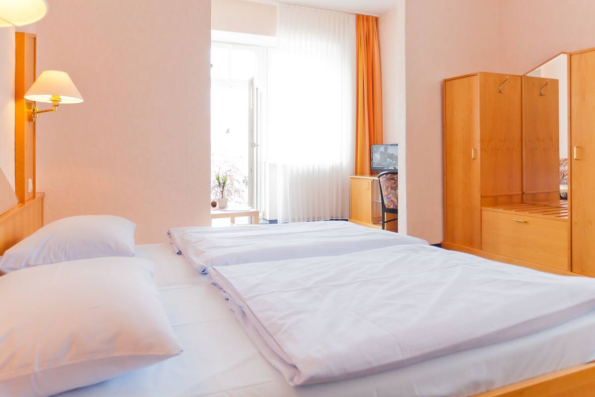 A hotel room with two beds, a wooden wardrobe, a television, and a window with curtains.