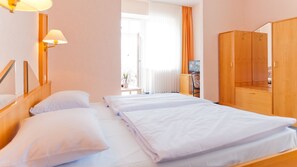 Una habitación de hotel con dos camas, un armario de madera, un televisor y una ventana con cortinas.
