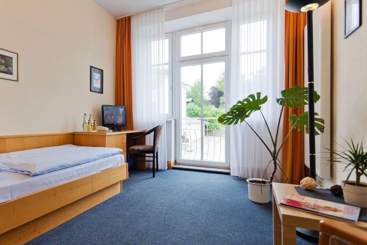 A hotel room with a bed, a desk with a computer, a chair, and a window with curtains.