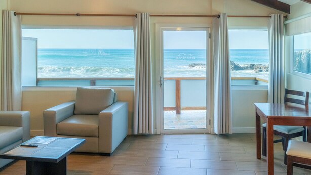 A room with a view of the ocean, a sofa, a table, and a ceiling fan. - Hotel Roca Sunzal (Tamanique)