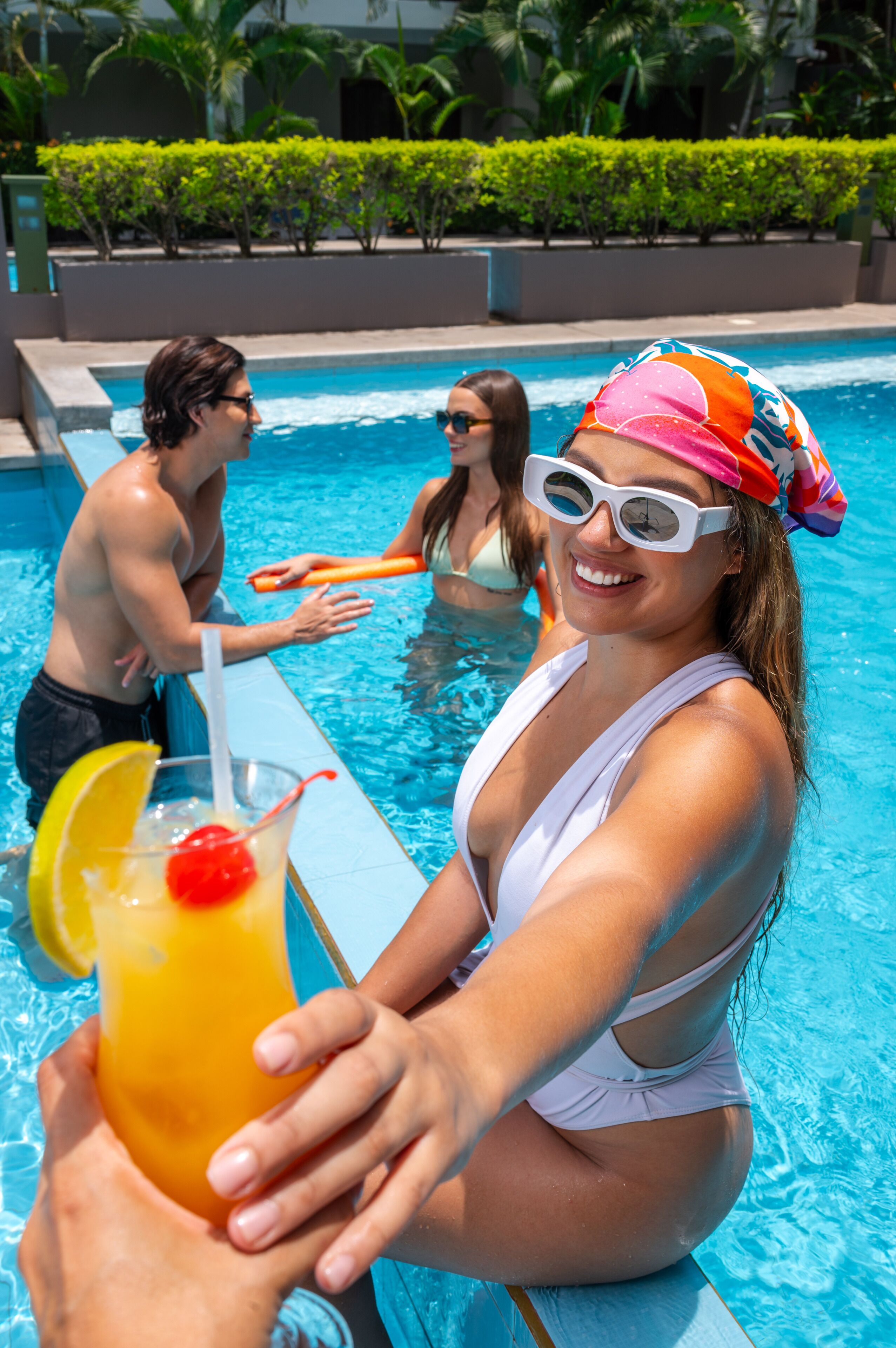 Une scène se déroulant au bord d’une piscine, avec des personnes en maillots de bain et une boisson décorée d’une cerise.