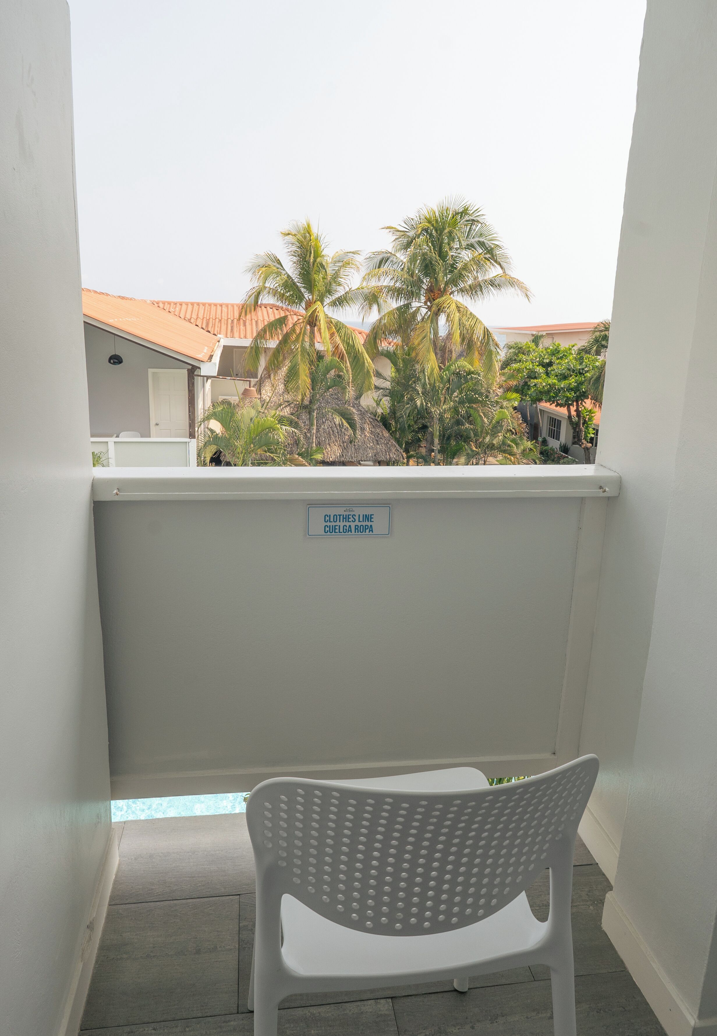 A white plastic chair on a balcony with a sign reading "CLOTHES LINE CUEGLA ROPA".