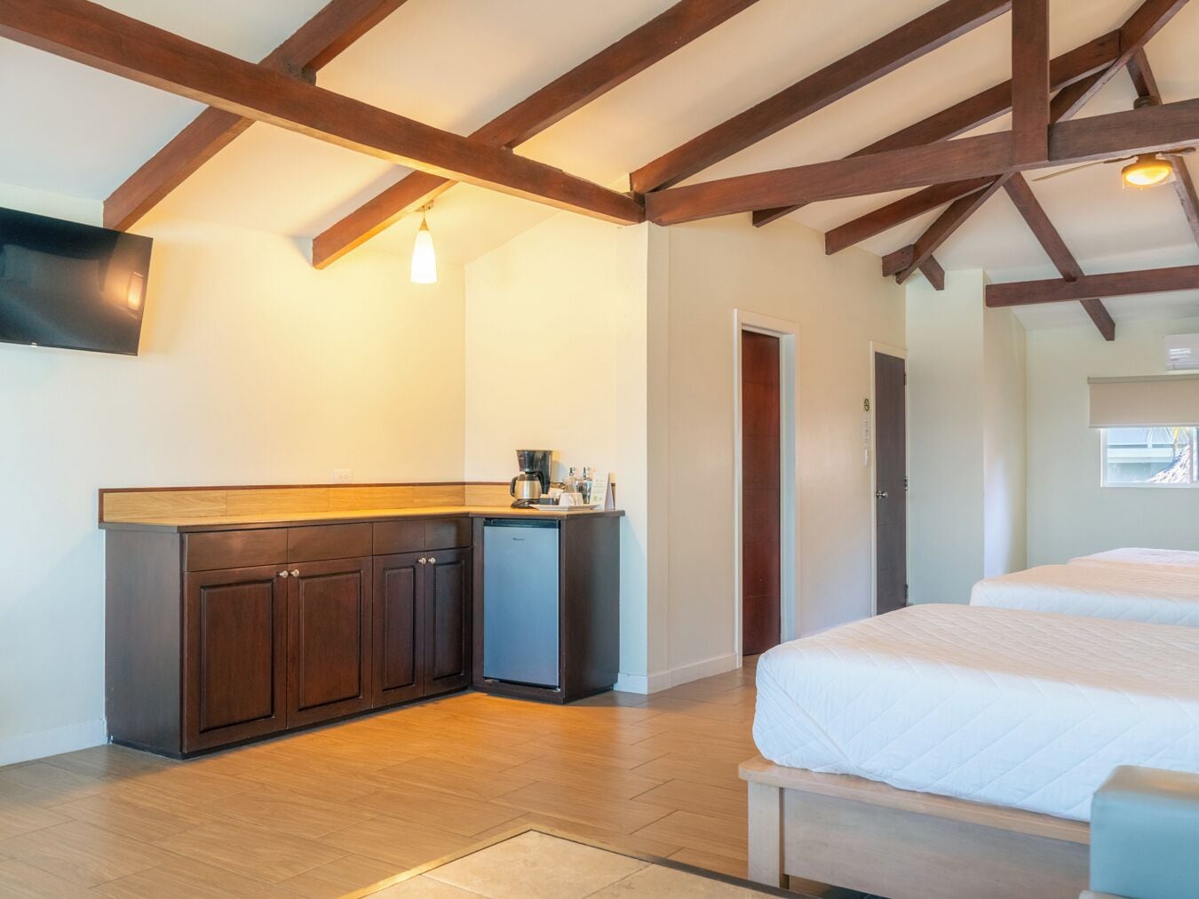 A room with a wooden ceiling, a built-in kitchen area, a bed, and a door leading to another room.