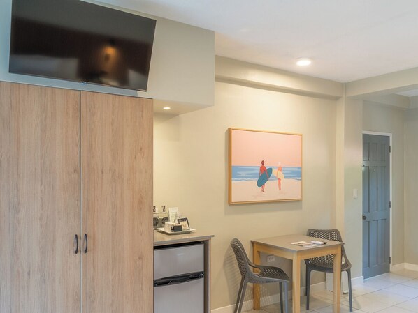 Una habitación con un armario de madera, un escritorio con sillas, un cuadro en la pared y una puerta al fondo.