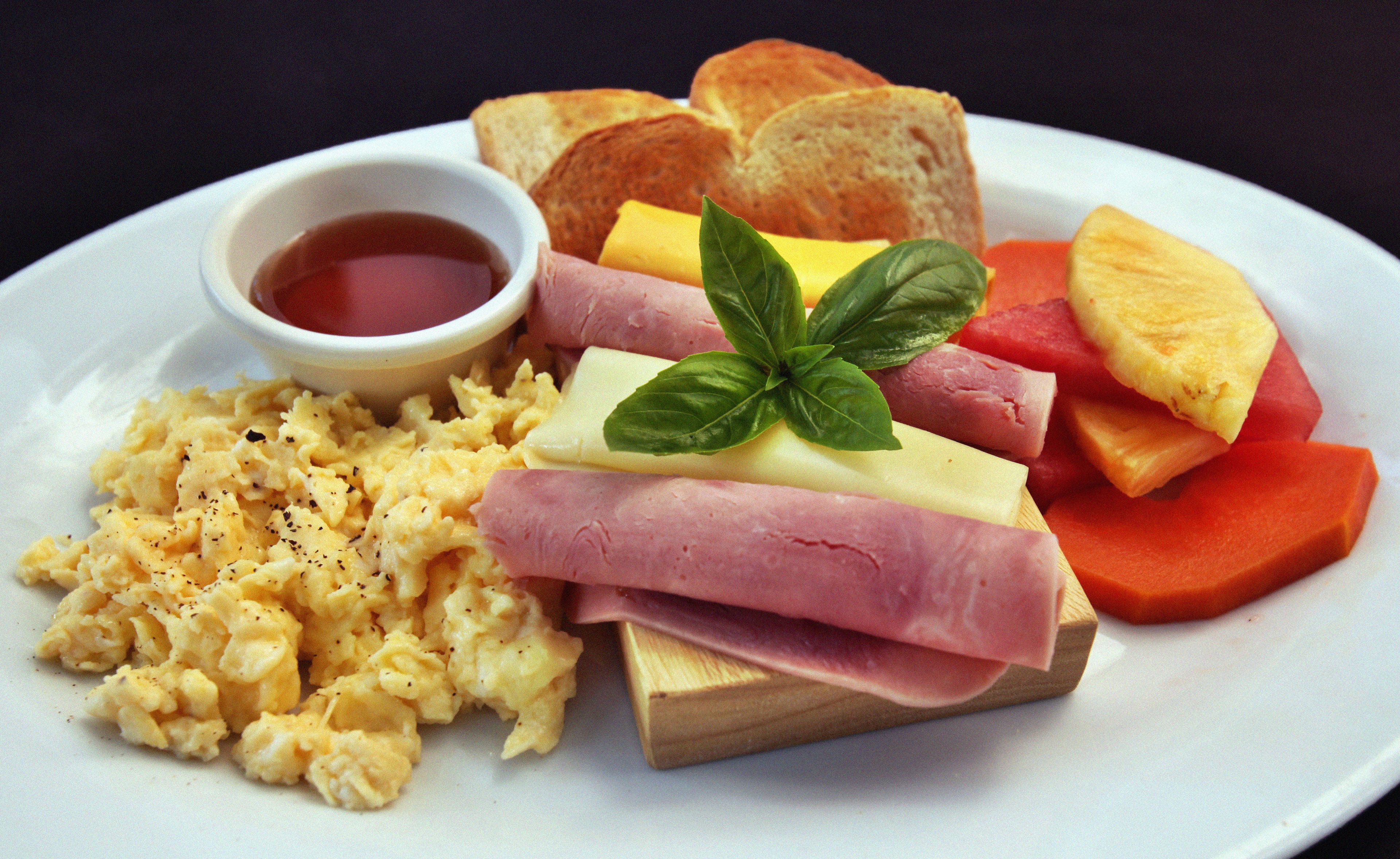 Ein Teller mit Rührei, Schinken, Käse, Toast und einer kleinen Schale Marmelade.
