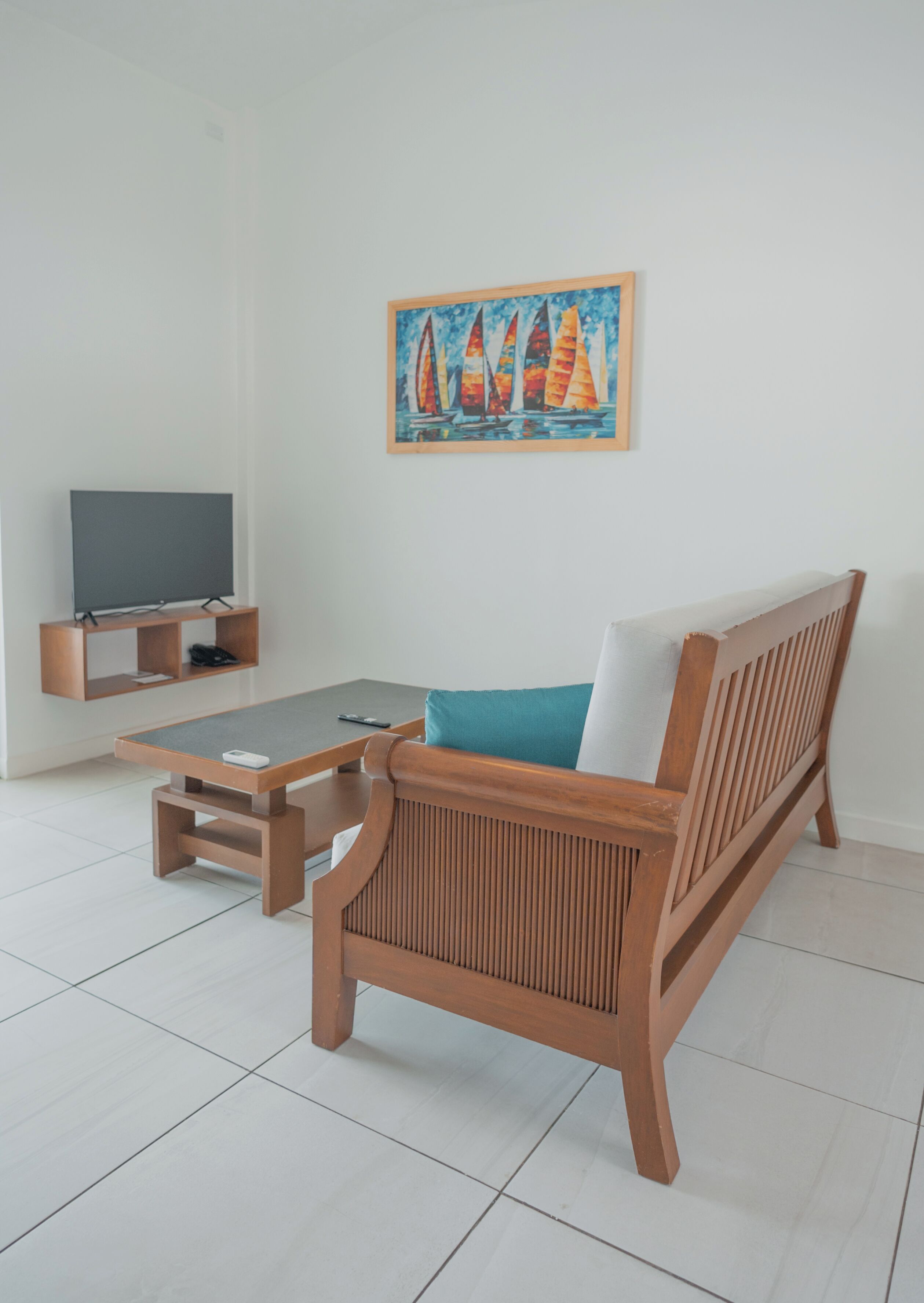 Ett modernt vardagsrum med en soffa i trä, ett soffbord och en platt-TV på ett TV-bord. En tavla med segelbåtar hänger på väggen.