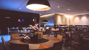 A modern restaurant with round tables, chairs, and a central floral arrangement. - Transamerica Fit Catalão (Catalao)
