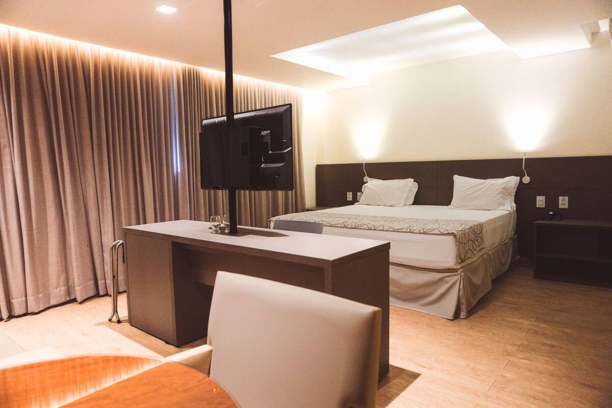 A hotel room with a bed, a desk, a chair, a television, and a window with curtains.