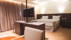 Una habitación de hotel con cama, escritorio, silla, televisión y ventana con cortinas.