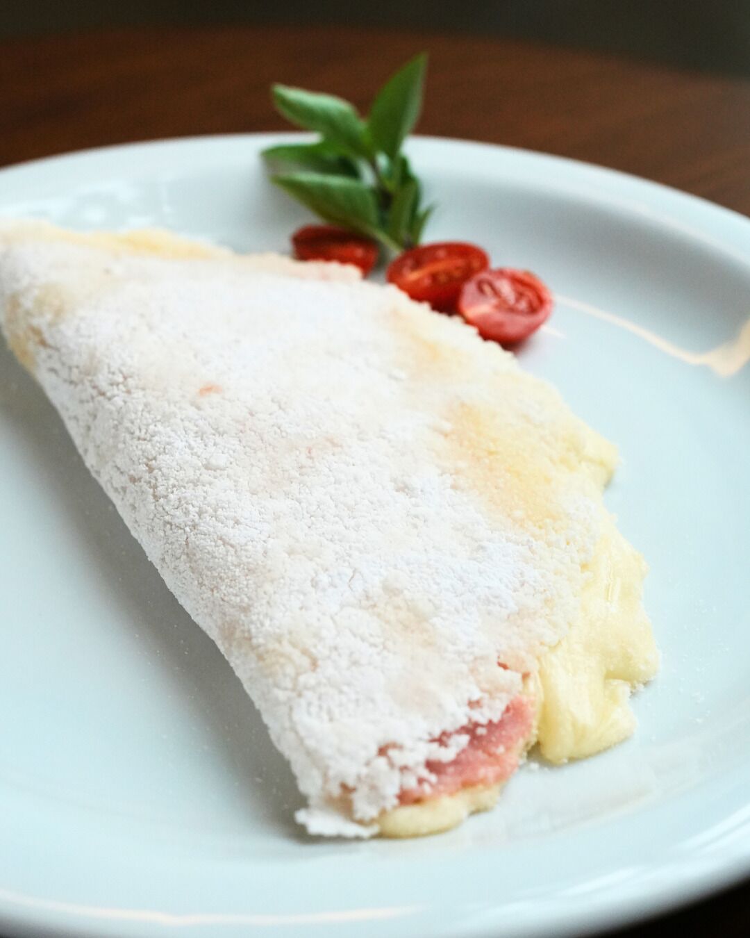 A rolled pastry with powdered sugar on a plate.