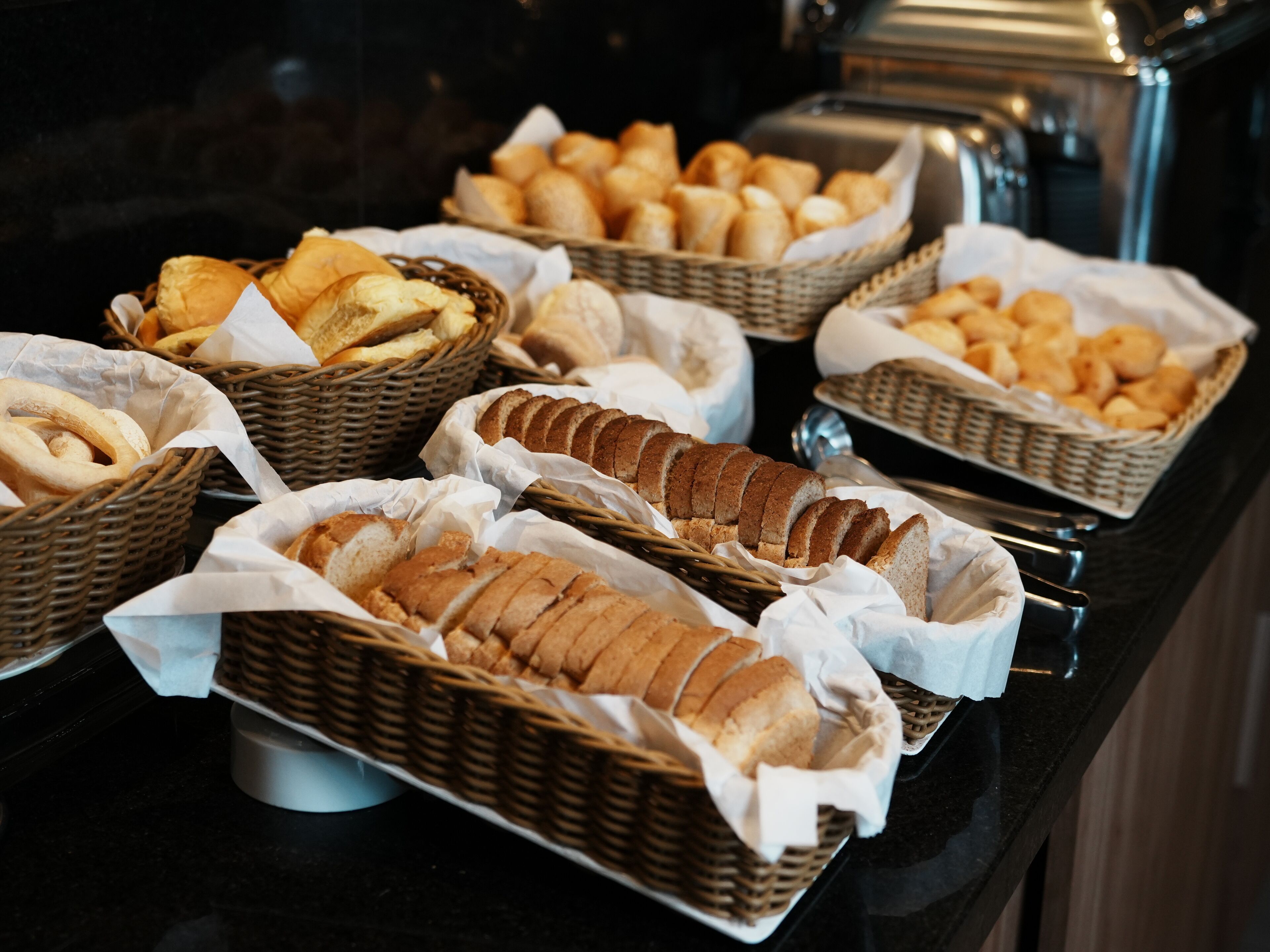 Un bufé con distintos tipos de pan y pasteles exhibidos en cestas de mimbre.