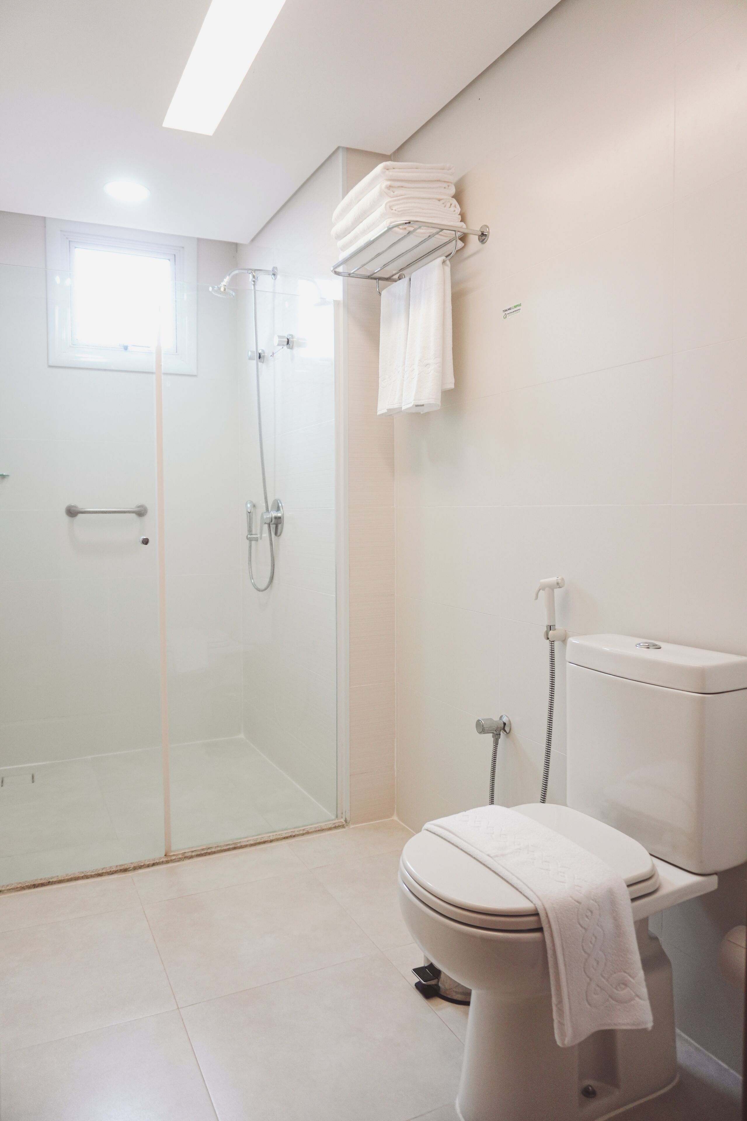 Un baño moderno con ducha envuelta en vidrio, un inodoro con una toalla sobre el asiento y un perchero en la pared.