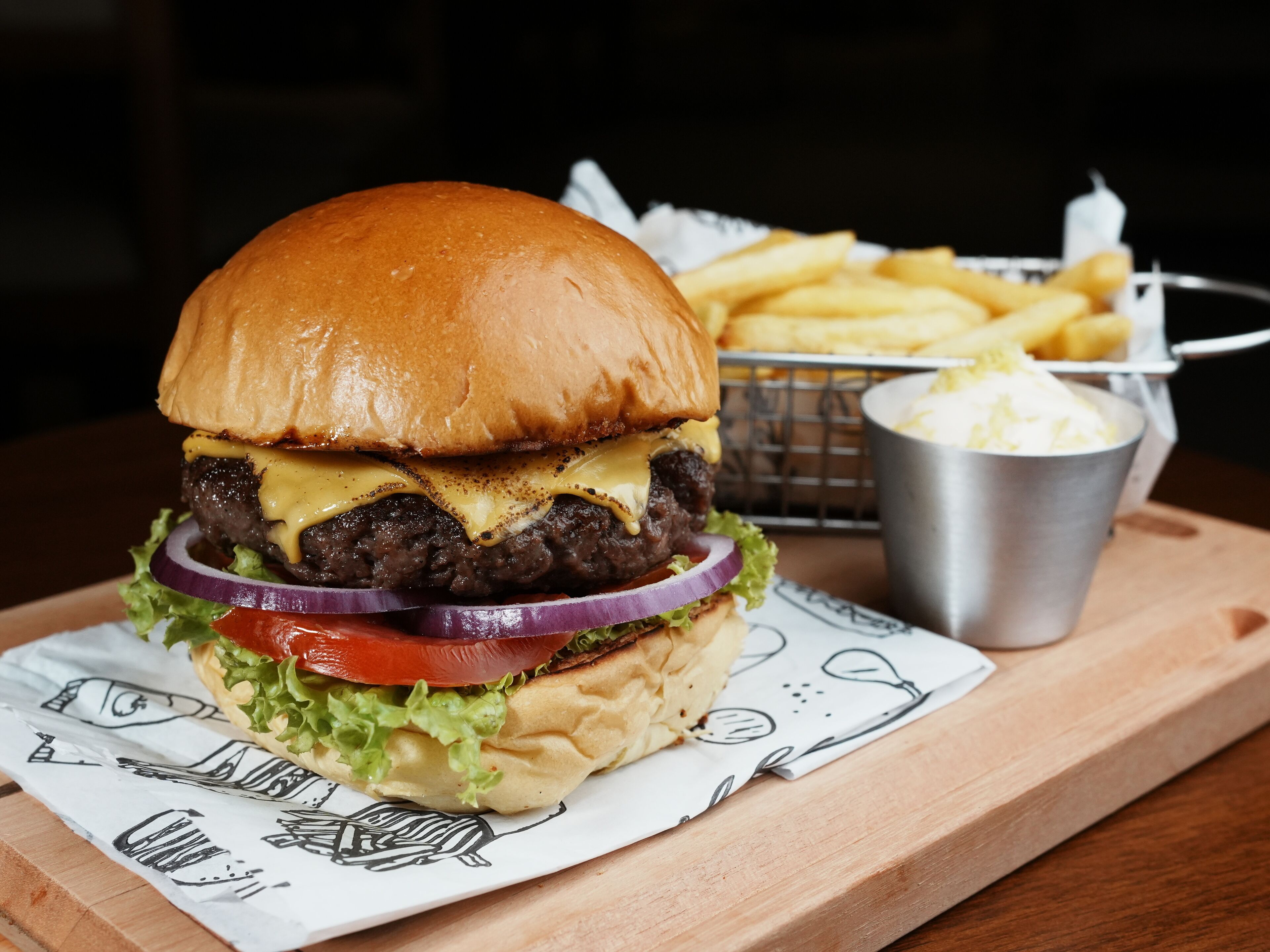 A burger with fries and a drink on a wooden table.