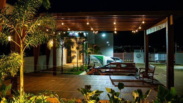 An outdoor covered area with a white van, wooden benches, and string lights. - Transamerica Fit Catalão (Catalao)