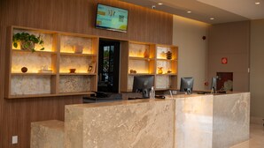 A reception desk with a digital screen, wooden shelving with decorative items, and a marble counter. - Transamerica Fit Catalão (Catalao)