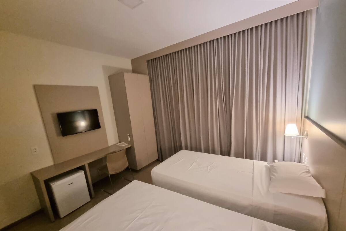 A hotel room with two beds, a TV, a desk, and a wardrobe.