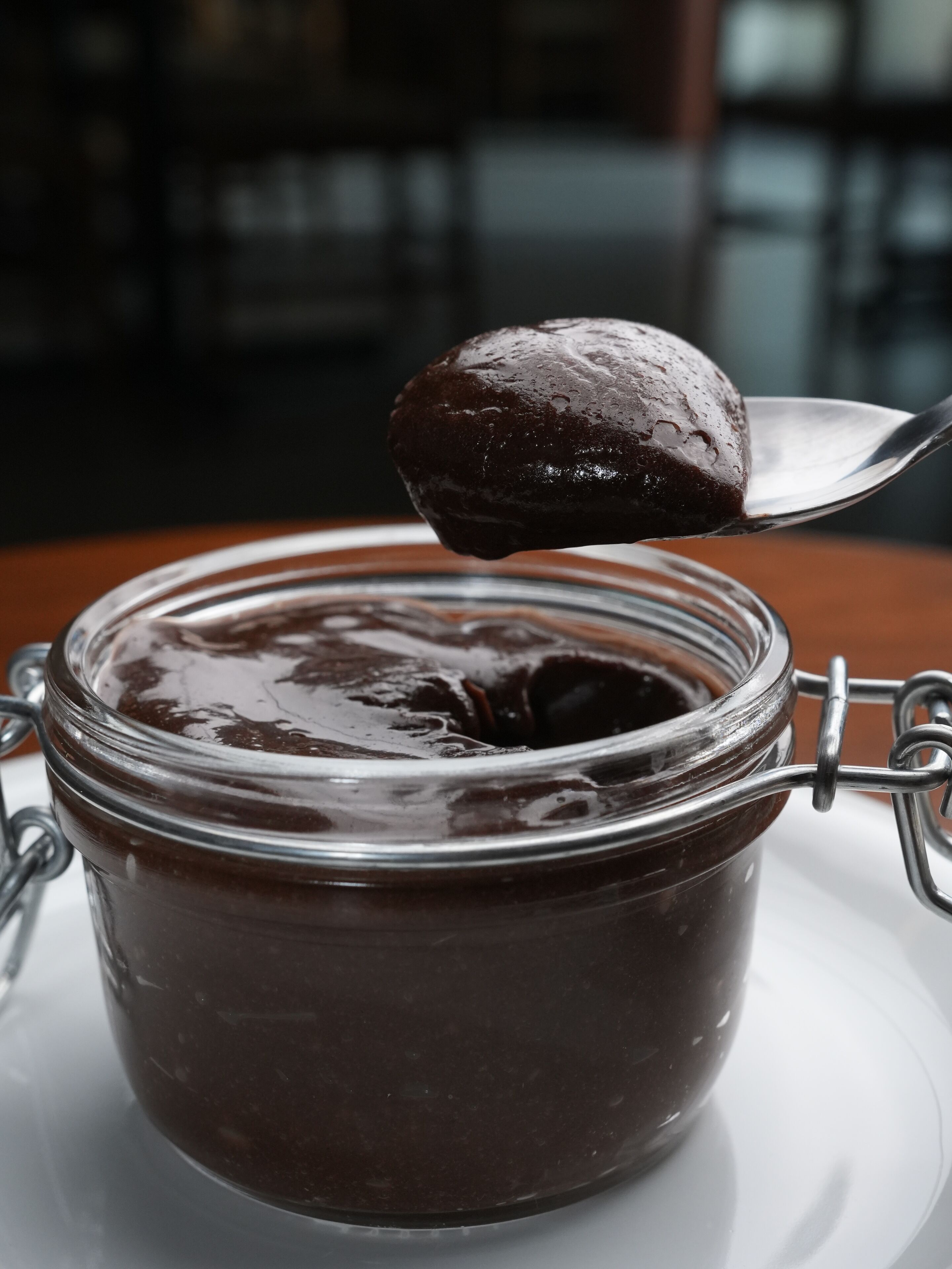 Une cuillère de confiture brun foncé dans un bocal en verre muni d’un couvercle à fermoir métallique.