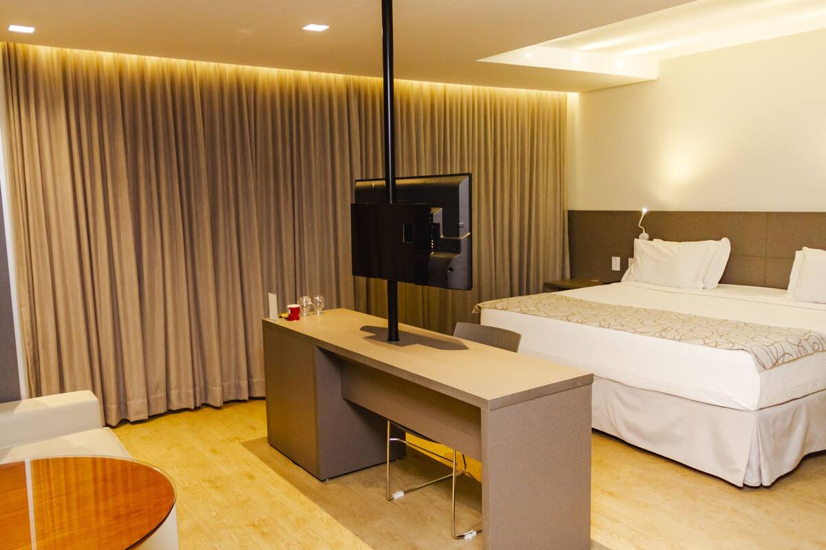 A hotel room with a bed, a desk, a television, and a curtain.