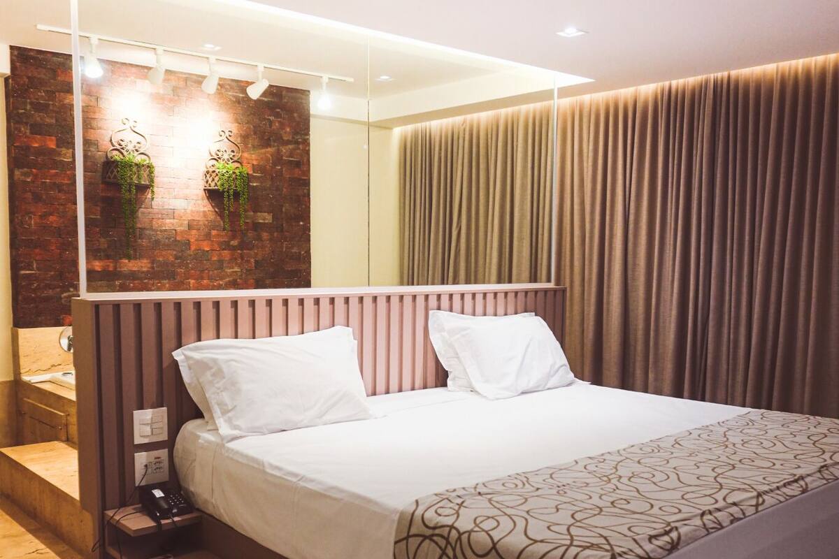 A modern hotel room with a bed, a nightstand, a mirror, and a brick accent wall.