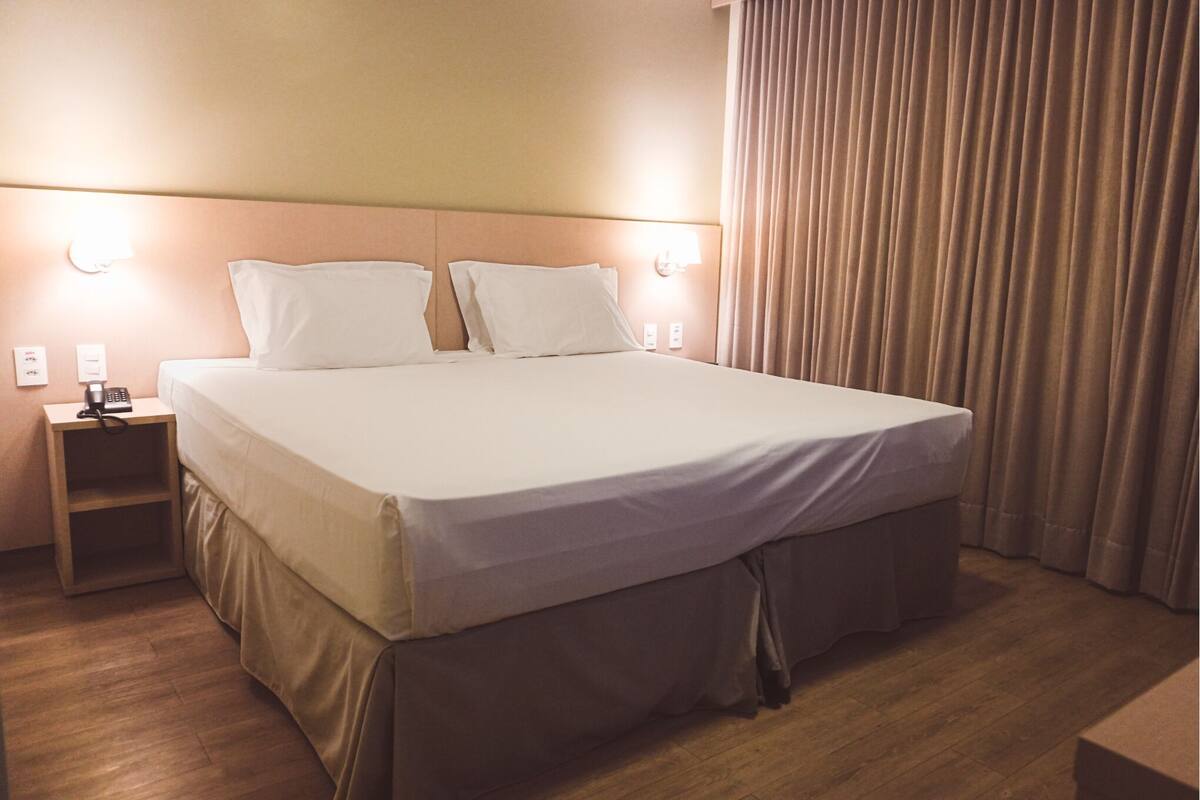 A neatly made bed with a headboard, a bedside table with a lamp, and a wooden nightstand.