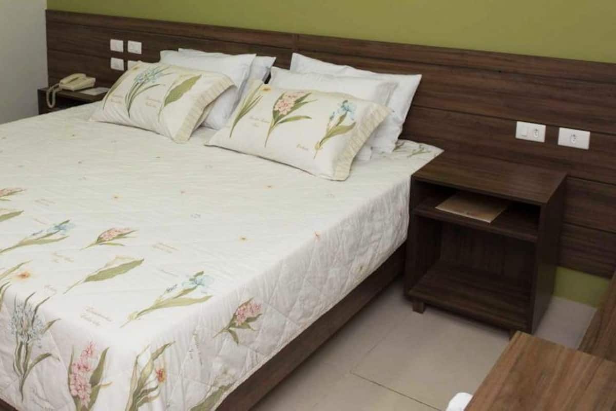Una cama bien hecha con ropa de cama floral, un cabecero de madera y una mesita de noche con una lámpara.