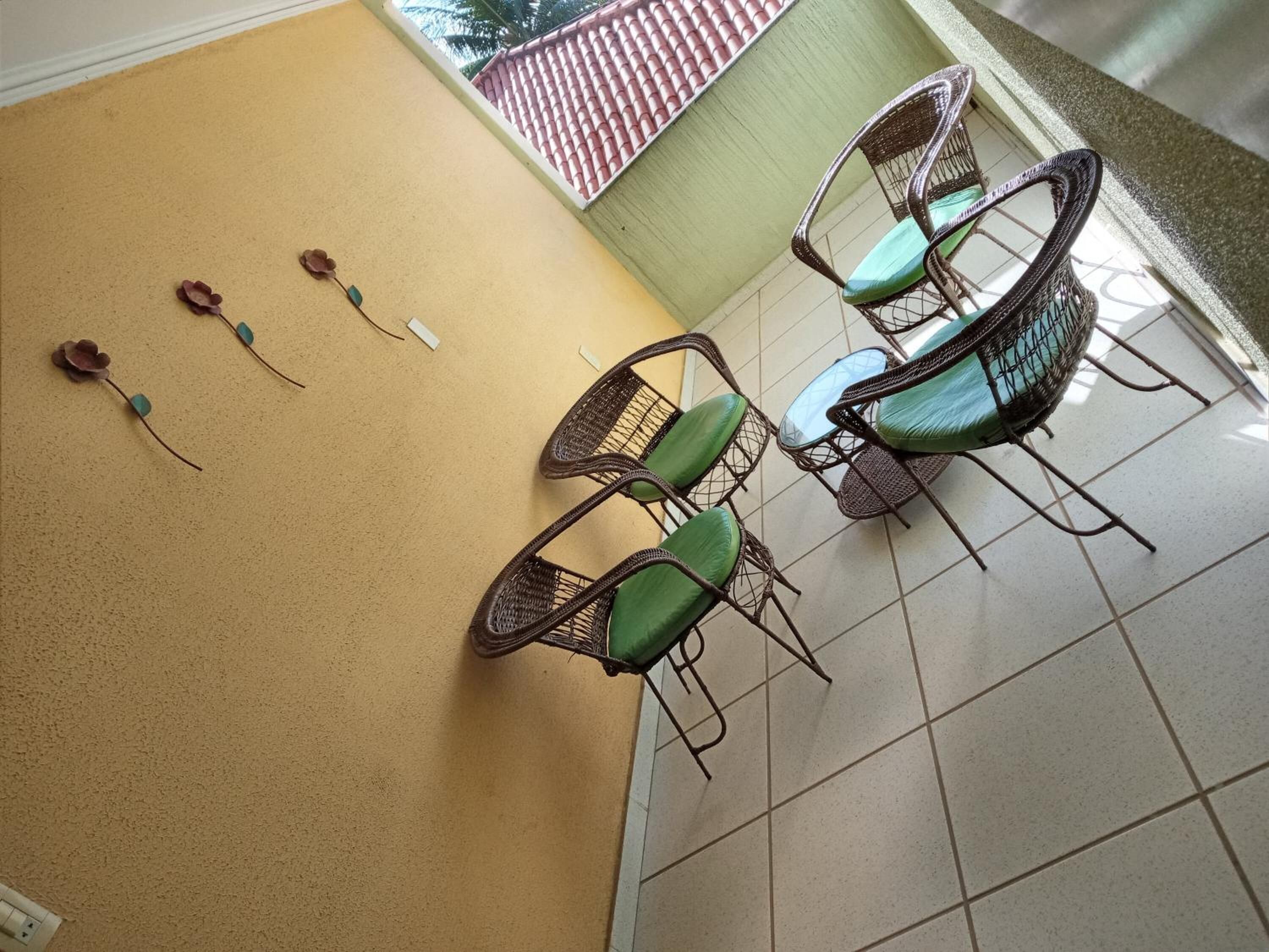 En balkon med fletstole og et lille bord, flisegulv og en væg med en pynteting.