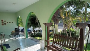 A covered outdoor area with a wooden swing, a green chair, and a table with chairs. - Pousada Aconchego (Juazeiro do Norte)