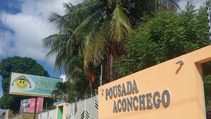 A building with a sign reading "Pousada Aconchego" and a signboard with a smiley face and text. - Pousada Aconchego (Juazeiro do Norte)