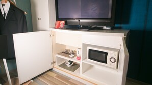 Une pièce équipée d’un téléviseur posé sur un meuble, d’un four à micro-ondes et d’une petite armoire contenant une bouilloire et des tasses.
