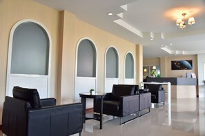 A modern hotel lobby with black leather seating, a reception desk, and large arched windows. - Book Place (Surat Thani)