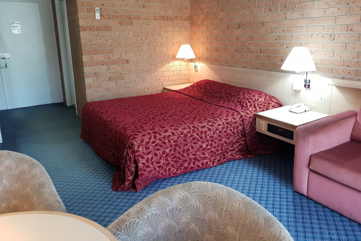 Ein Hotelzimmer mit einem Bett, zwei Nachttischlampen, einem Nachttisch, einem Sessel und einer Tür.