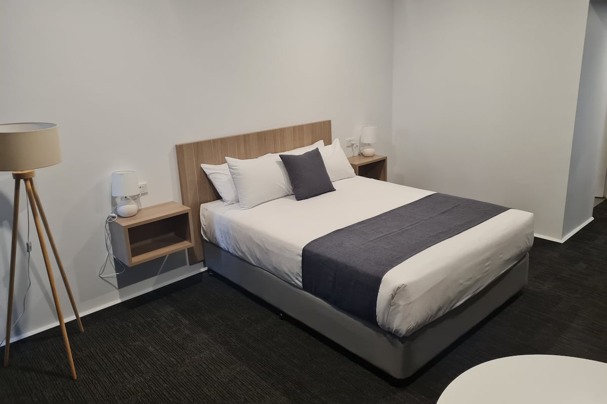 Ein modernes Hotelzimmer mit einem großen Bett, Nachttischen, einer Stehlampe und einer zusätzlichen Lampe auf dem Nachttisch.