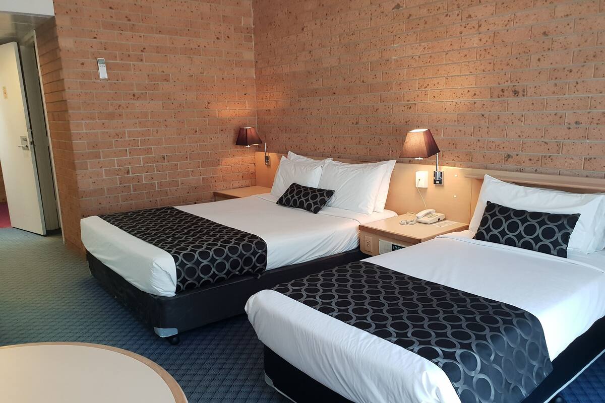 Ein Hotelzimmer mit zwei Betten, einem Schreibtisch, einem Stuhl und einer Ziegelwand.