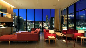 Un moderno vestíbulo de hotel con vistas a la ciudad, asientos rojos y un ventanal grande.