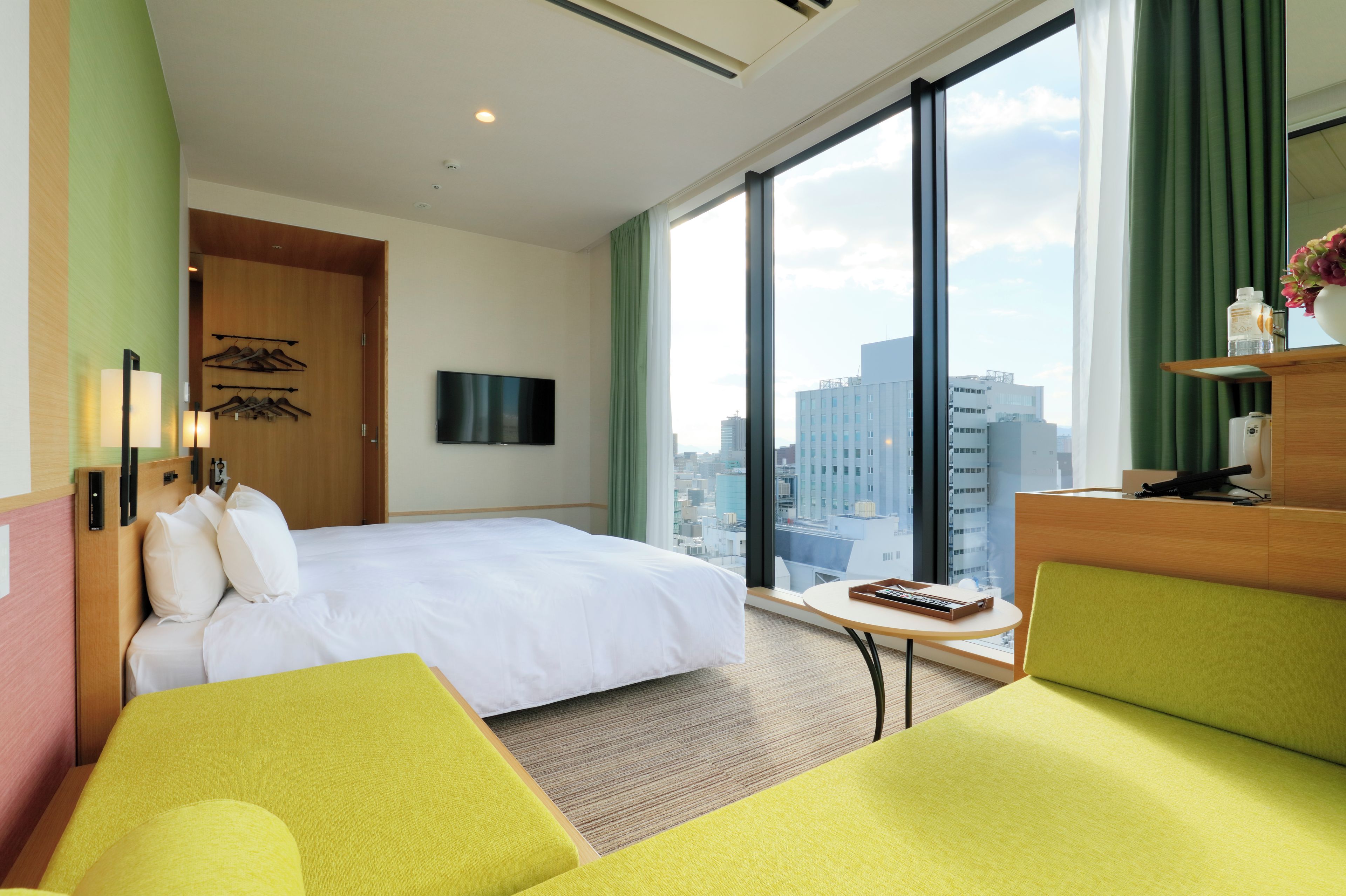 Habitación de hotel con cama, escritorio, silla, televisor y vista a la ciudad.