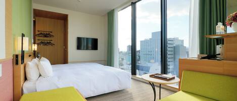 Habitación de hotel con cama, escritorio, silla, televisor y vista a la ciudad.