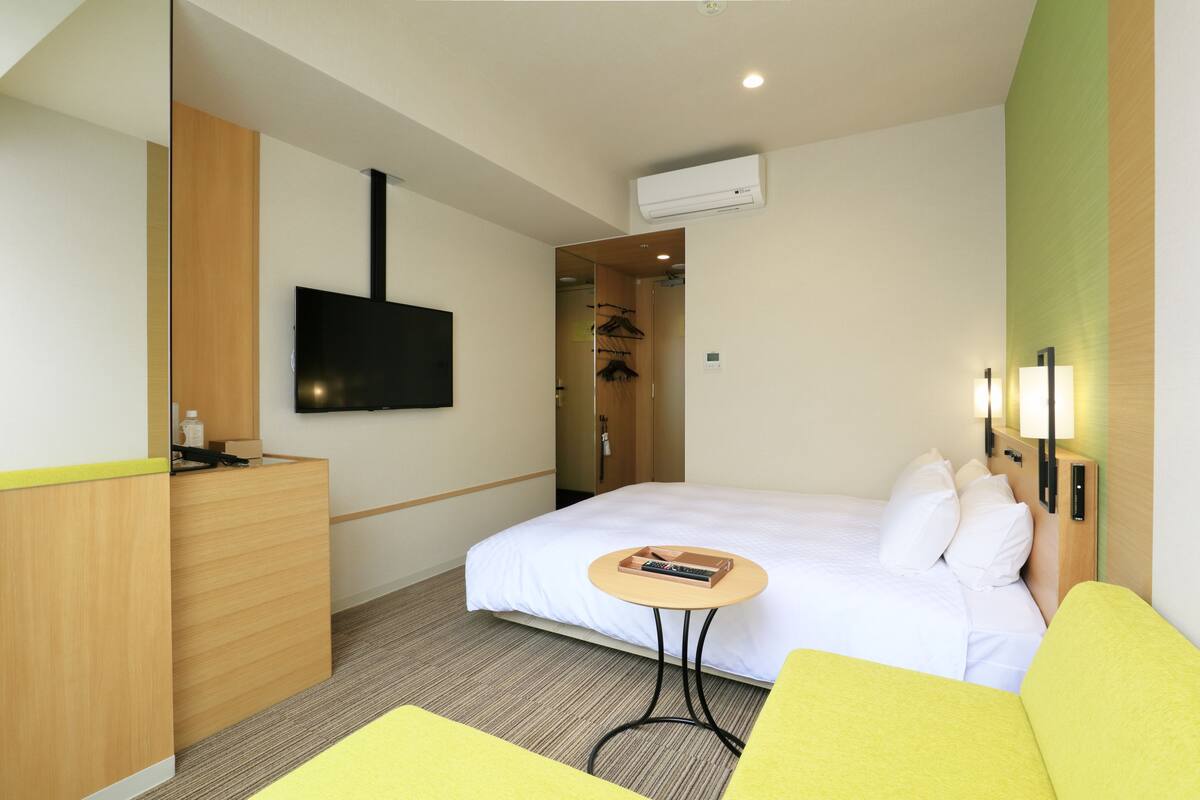 Una habitación de hotel con una cama, una mesita pequeña, un televisor y un armario.