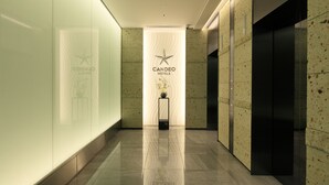 Un lobby moderno de hotel con pared de vidrio, un mostrador de recepción y un cartel de Candeo Hotels.