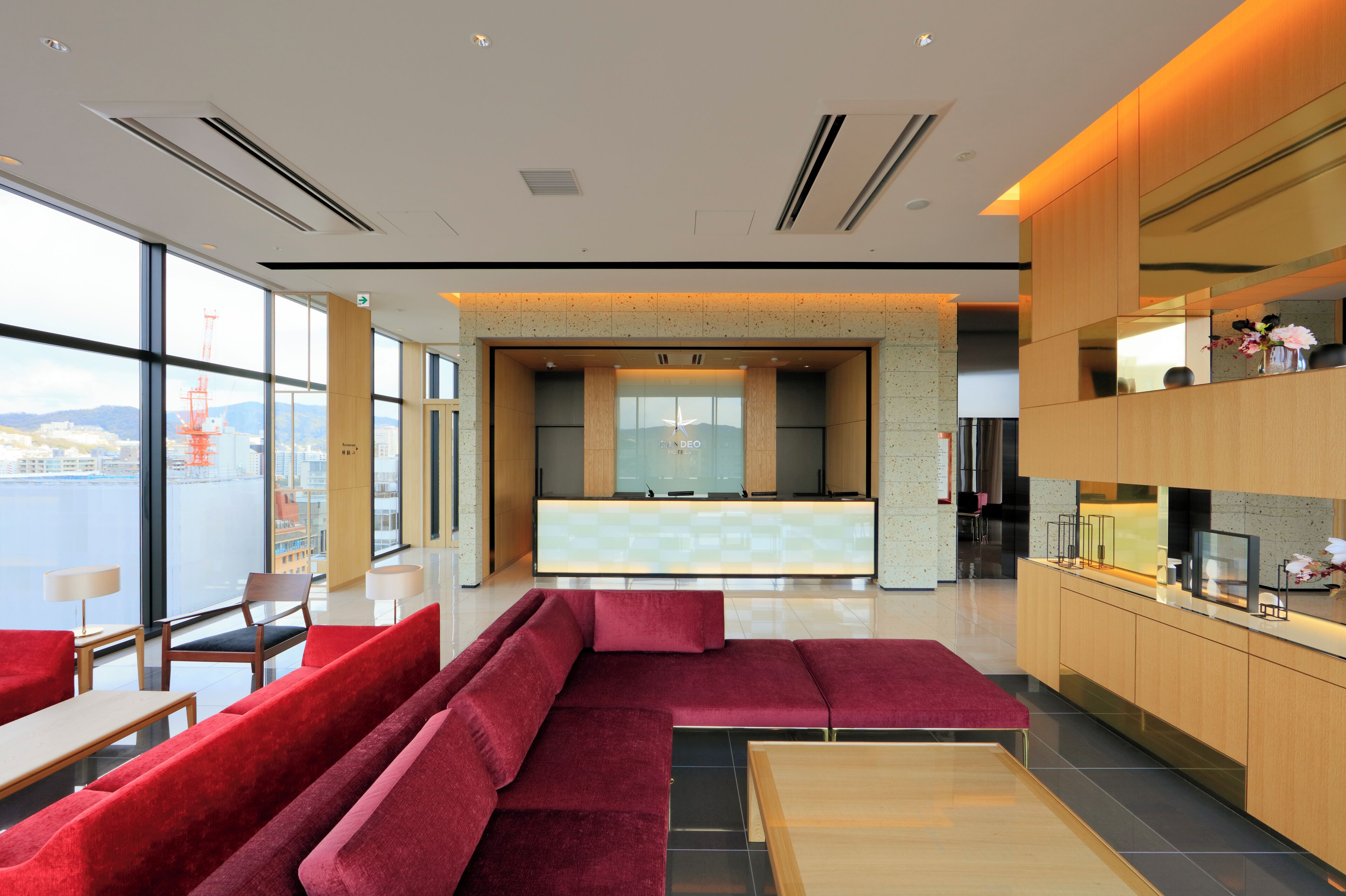 A modern hotel lobby with a seating area, a reception desk, and a view of the city.