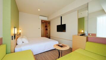 Habitación de hotel con cama, una pequeña mesa, un sofá, televisor montado en la pared y un espejo.