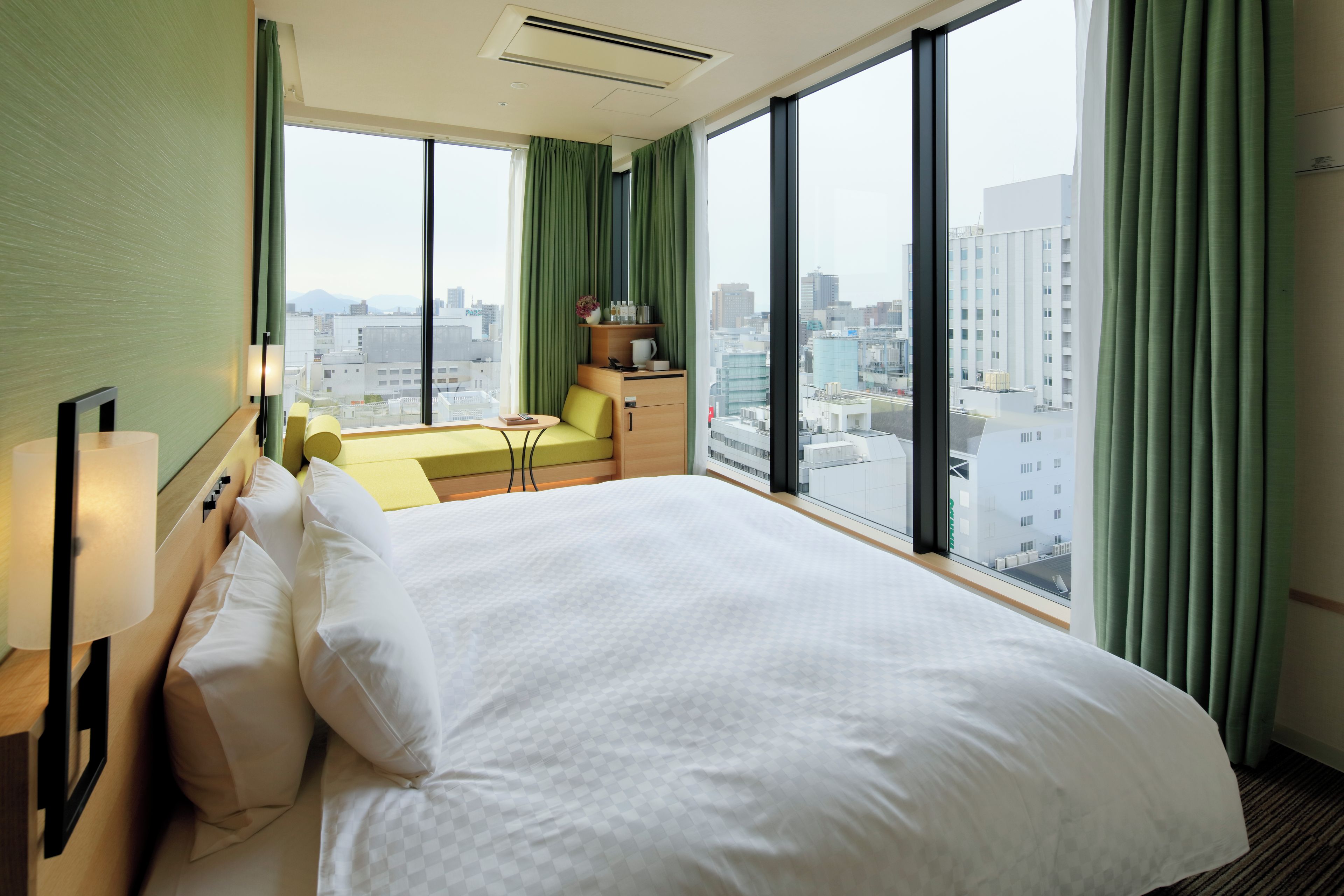 A hotel room with a large bed, a desk, a chair, and a view of the cityscape.