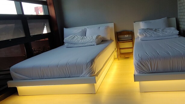 Dos camas individuales con ropa de cama blanca, mesitas de noche de madera y una pared de ladrillo.