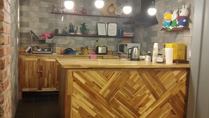 Una cocina con armarios de madera, pared de ladrillo y estantes con electrodomésticos y objetos decorativos.
