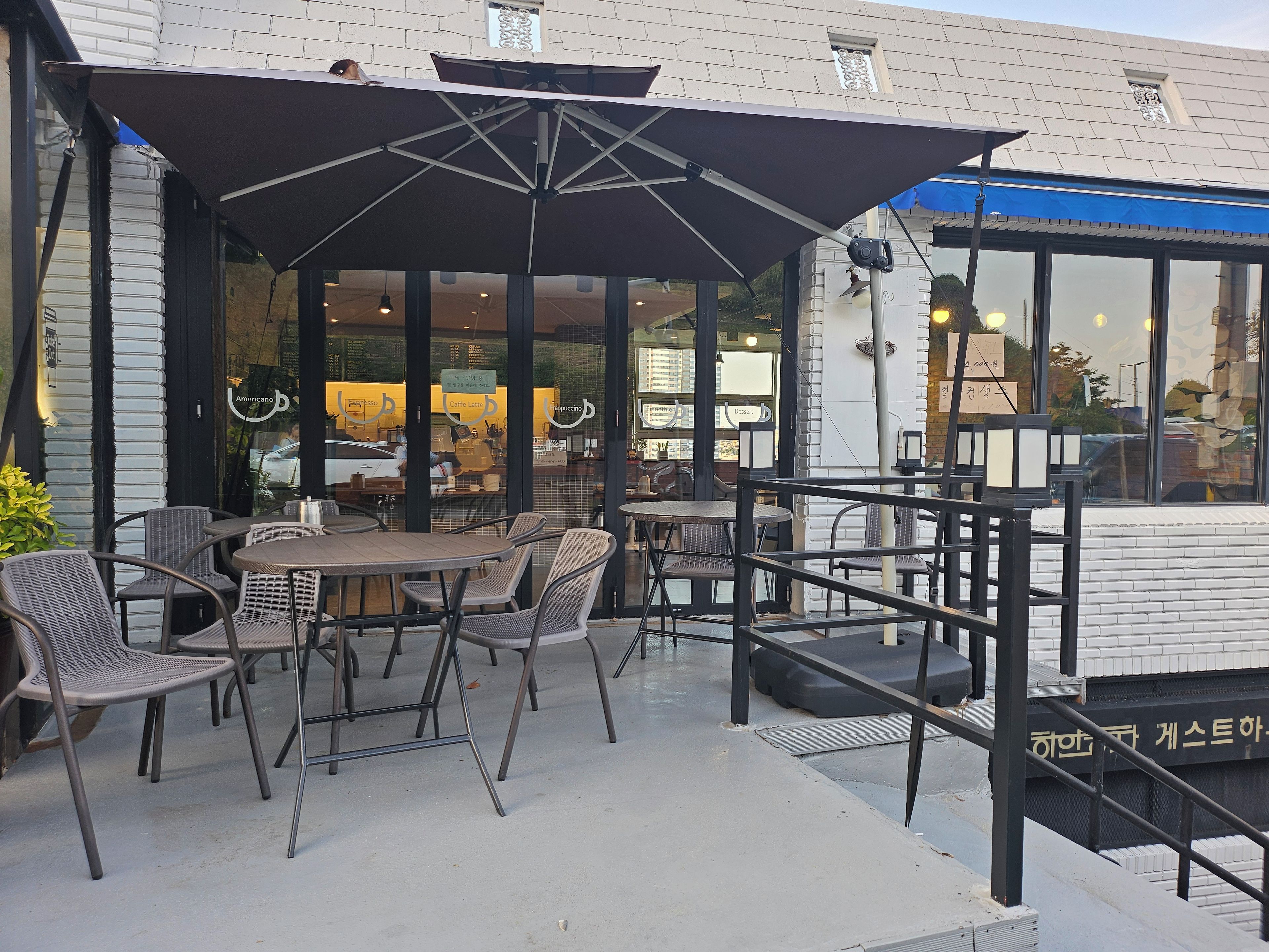An outdoor seating area with tables and chairs, a covered section with umbrellas, and a building with large windows and signage.