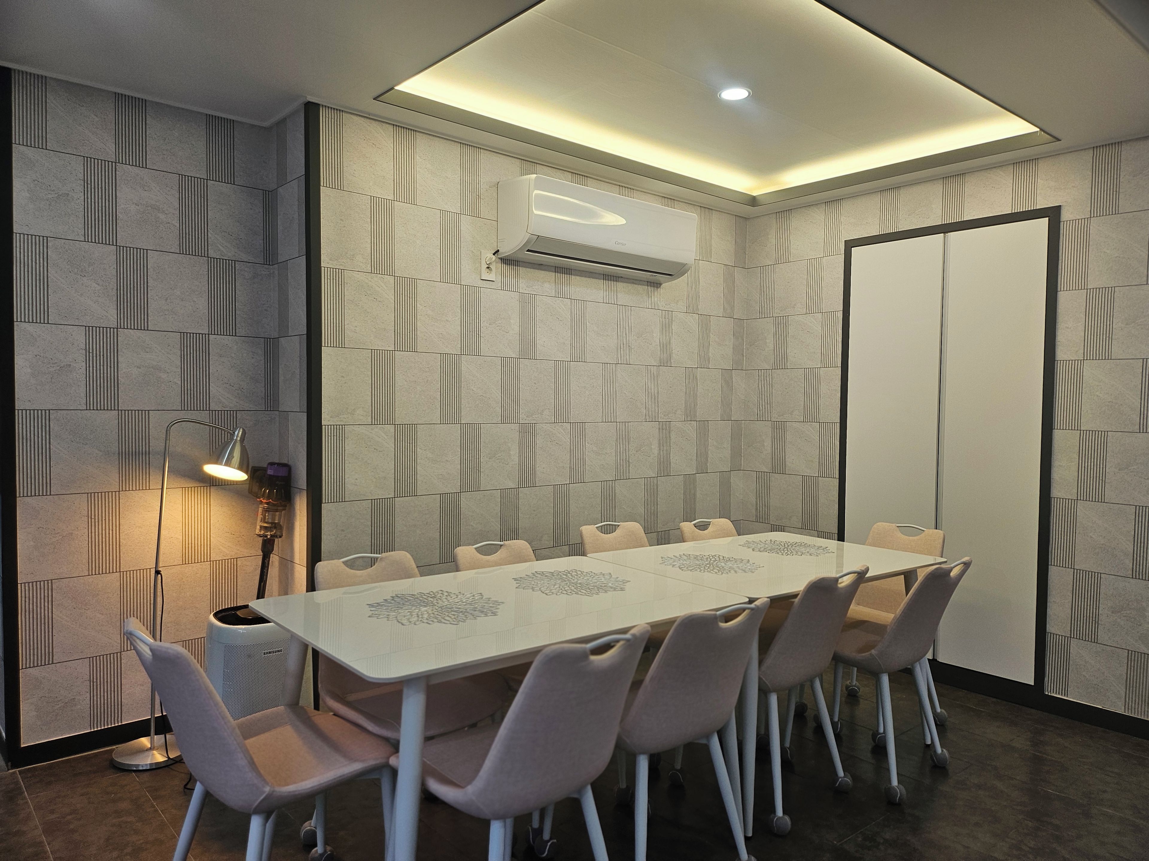 Un salón de conferencias con una larga mesa y sillas, un equipo de aire acondicionado y una lámpara.