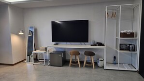 Una sala de estar moderna con un televisor de pantalla plana, un escritorio, dos taburetes, un pequeño armario y una estantería.