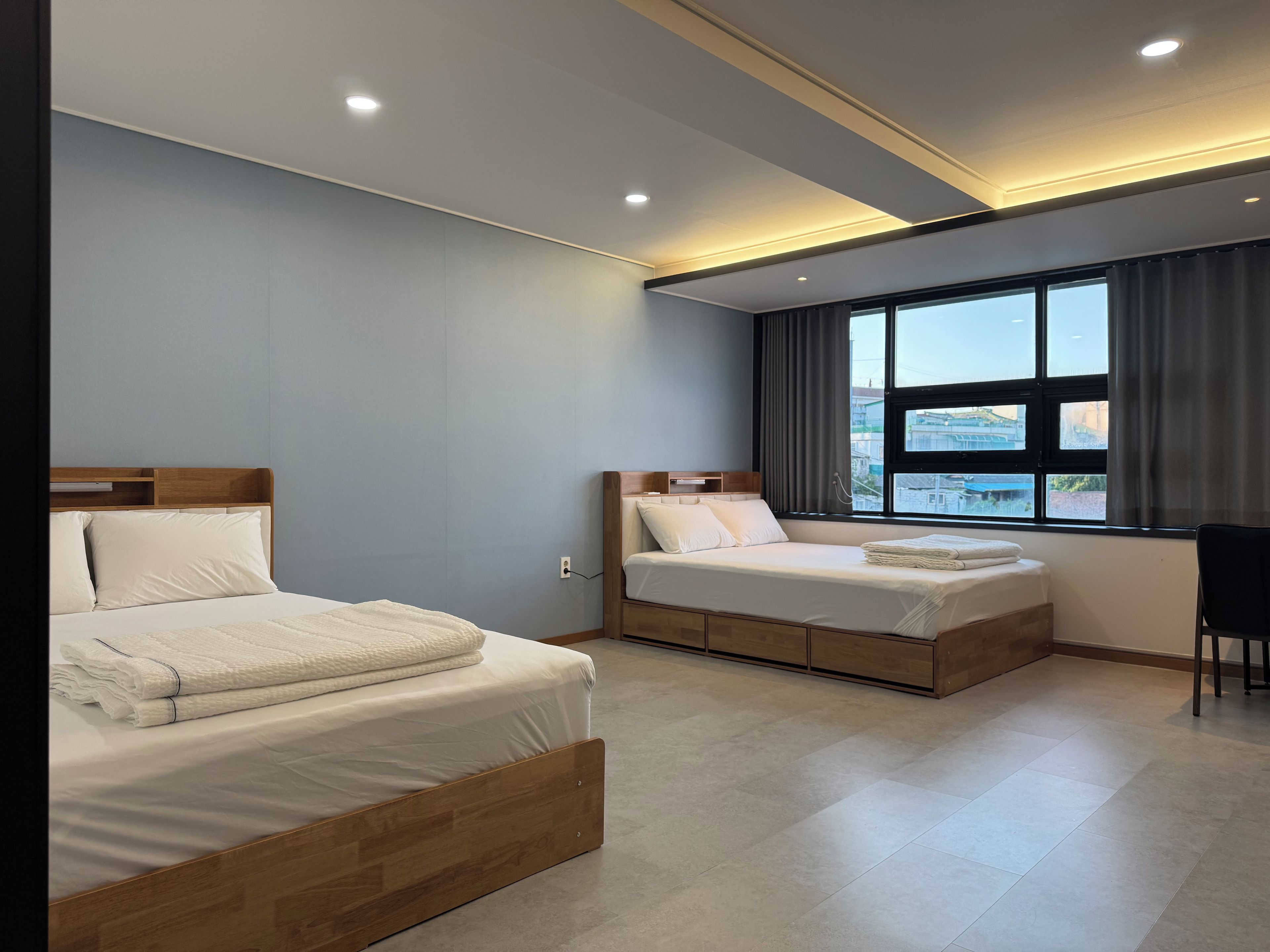 A modern hotel room with two beds, a large window, and a view of the cityscape.