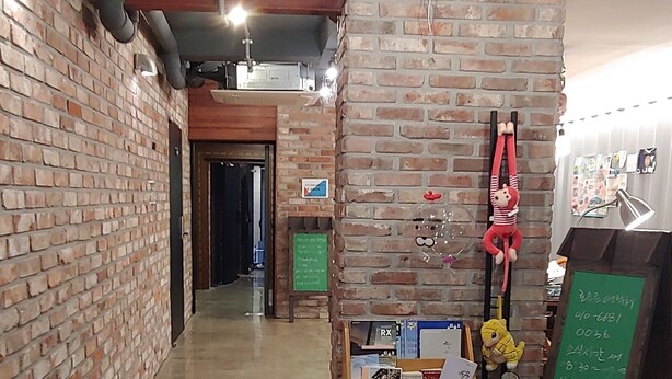 Un couloir aux murs de briques, doté d’un plancher ciré et d’un comptoir d’accueil avec une enseigne verte.