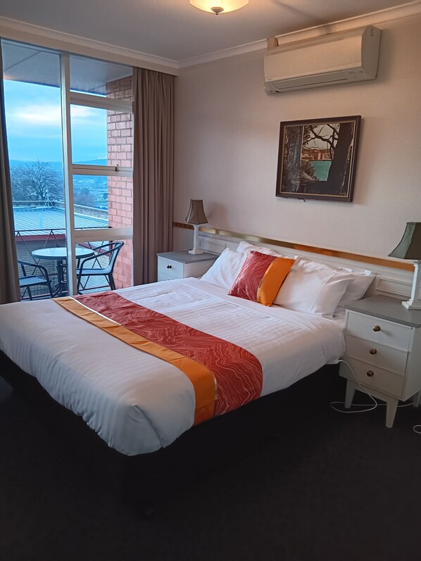 A hotel room with a large bed, a nightstand, a lamp, a picture on the wall, and a view through a sliding glass door. - Parklane Motel (Launceston)