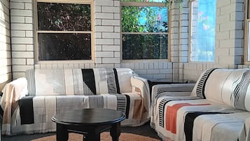 Ein Zimmer mit Backsteinwand, zwei Rundbogenfenstern, einer Couch, einem Tisch und einer hängenden Pflanze.